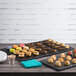 An Elite Global Solutions faux black slate melamine serving board on a table with a variety of desserts and snacks.