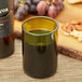 An Arcoroc green wine bottle tumbler filled with wine next to a bottle of wine.