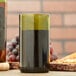 A green Arcoroc wine bottle tumbler filled with wine next to a bottle of wine.