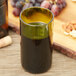 A close up of a green Arcoroc wine bottle tumbler filled with wine on a table with grapes and nuts.