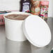 A close up of a white Choice paper food container with a lid on a counter.