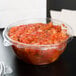 A Dart plastic bowl of salsa on a table.