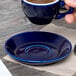 A hand holding a blue Tuxton cappuccino cup above a blue Tuxton saucer.