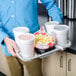 A man using a Huhtamaki Chinet take-out tray with white cups and a white container filled with pink liquid and popcorn.