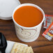 A Solo Symphony paper soup cup with a lid full of soup on a table with crackers.