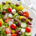 A plate of salad with tomatoes, olives, and cheese.