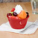 A red Thunder Group melamine bouillon bowl filled with fruit and whipped cream with a fork.
