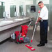 A man using an Unger red mop bucket with side-press wringer to mop the floor.