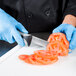 A gloved hand uses a Dexter-Russell V-Lo scalloped utility knife to cut a tomato.