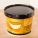 A Huhtamaki black and white paper soup container with a black lid.