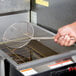 A hand holding a Thunder Group metal mesh skimmer over a fryer.