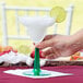 A hand holding a Fineline Flairware plastic margarita with a green base and lime wedge.