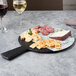An Elite Global Solutions slate and marble serving board with cheese and crackers on a table with a glass of wine.