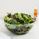 A bowl of salad with green leaves in a clear Fineline PET plastic bowl.