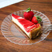A slice of cheesecake with strawberries on a clear plastic plate with a fork.
