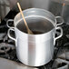 A large silver Vollrath double boiler on top of a stove with a wooden spoon in it.