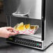 A person using an Amana commercial microwave to heat a tray of chips.