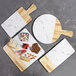 An Elite Global Solutions faux alder wood and marble round serving board with handle on a table with cheese and cutting boards.