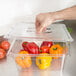 A hand putting a Carlisle clear plastic lid on a clear plastic container of yellow bell peppers.