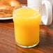 A Libbey English Pub glass filled with orange juice on a table with a bagel and coffee.