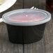 A black plastic Newspring oval souffle container with a clear lid.