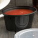 A black Newspring oval souffle cup with clear lid filled with red sauce.
