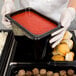 A person in gloves holding a Cambro high heat plastic food pan full of food.