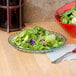 A bowl of salad with a fork in it on a table with a Mediterranean jade polycarbonate bowl.