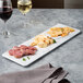 An Elite Global Solutions faux Carrara marble rectangular serving board with food and wine on it.