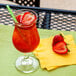 A Libbey Poco Grande glass of red liquid with ice and a straw on a napkin with strawberries.