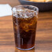 A clear Cambro plastic tumbler filled with soda and ice on a table with a bowl of chips.