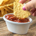 A hand holding a chip dips it into a bowl of salsa on a table.
