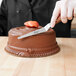 A hand holding an Ateco offset icing spatula over a chocolate cake.