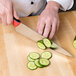 A person cutting cucumbers on a cutting board with a Mercer Culinary Millennia Colors chef knife with a red handle.