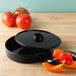 A black round HS Inc. tortilla server with a lid on a table next to tomatoes and peppers.