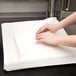 A person's hands on a stack of Hoffmaster white flat pack linen-feel napkins.