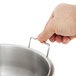 A hand holding a Vollrath stainless steel container over a silver bowl.