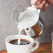 A person using a Tablecraft stainless steel bell creamer to pour milk into a cup of coffee.