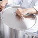 A person holding a Vollrath stainless steel domed lid over a large pot.