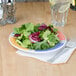 A GET Diamond Barcelona wide rim melamine plate with salad and a fork on a table.