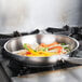 A Vollrath stainless steel fry pan with vegetables cooking in it on a stove.