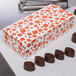 A 1 lb. Leaf Candy Box with orange and white leaves on the counter next to chocolates.