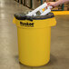 A person holding a yellow Continental 32 gallon trash can.