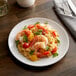 A plate of shrimp and rice with tomatoes and herbs on a white Acopa stoneware plate on a table.