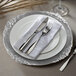 A silverware set on a silver leaf embossed charger plate.