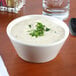 A Tuxton eggshell white china soup bowl filled with soup and garnished with parsley.