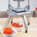 A Nemco Easy Chopper II vegetable slicer cutting tomatoes on a counter with bowls of tomatoes.