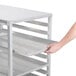A hand places a tray in an Advance Tabco sheet pan rack on a table.