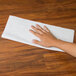A hand holding a white Chicopee DuraWipe shop towel on a table.
