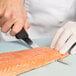 A person in gloves using a Victorinox Flexible Narrow Boning Knife to cut a piece of salmon.